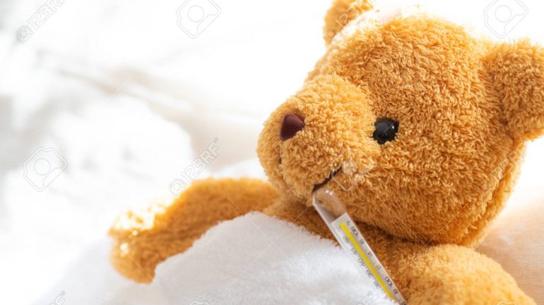 Teddy bear lyiing sick in hospital bed with with thermometer and